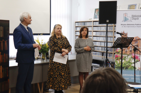 troje ludzi stojących przed publicznością w tle regały z płytami, ekran oraz rollup biblioteczny