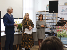 troje ludzi stojących przed publicznością w tle regały z płytami, ekran oraz rollup biblioteczny