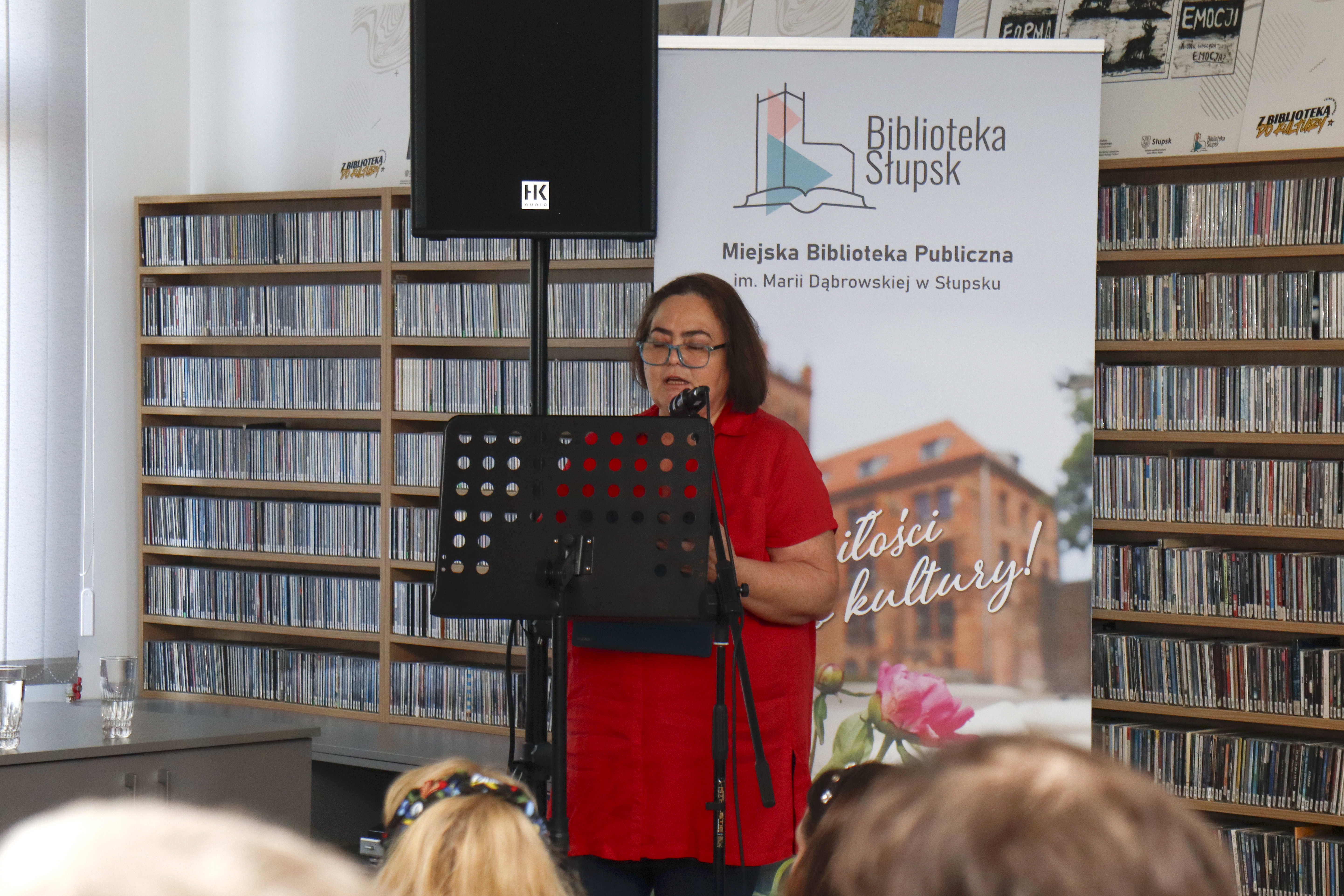 kobieta stojąca na tle rollupu biblioteki i regałach z płytami