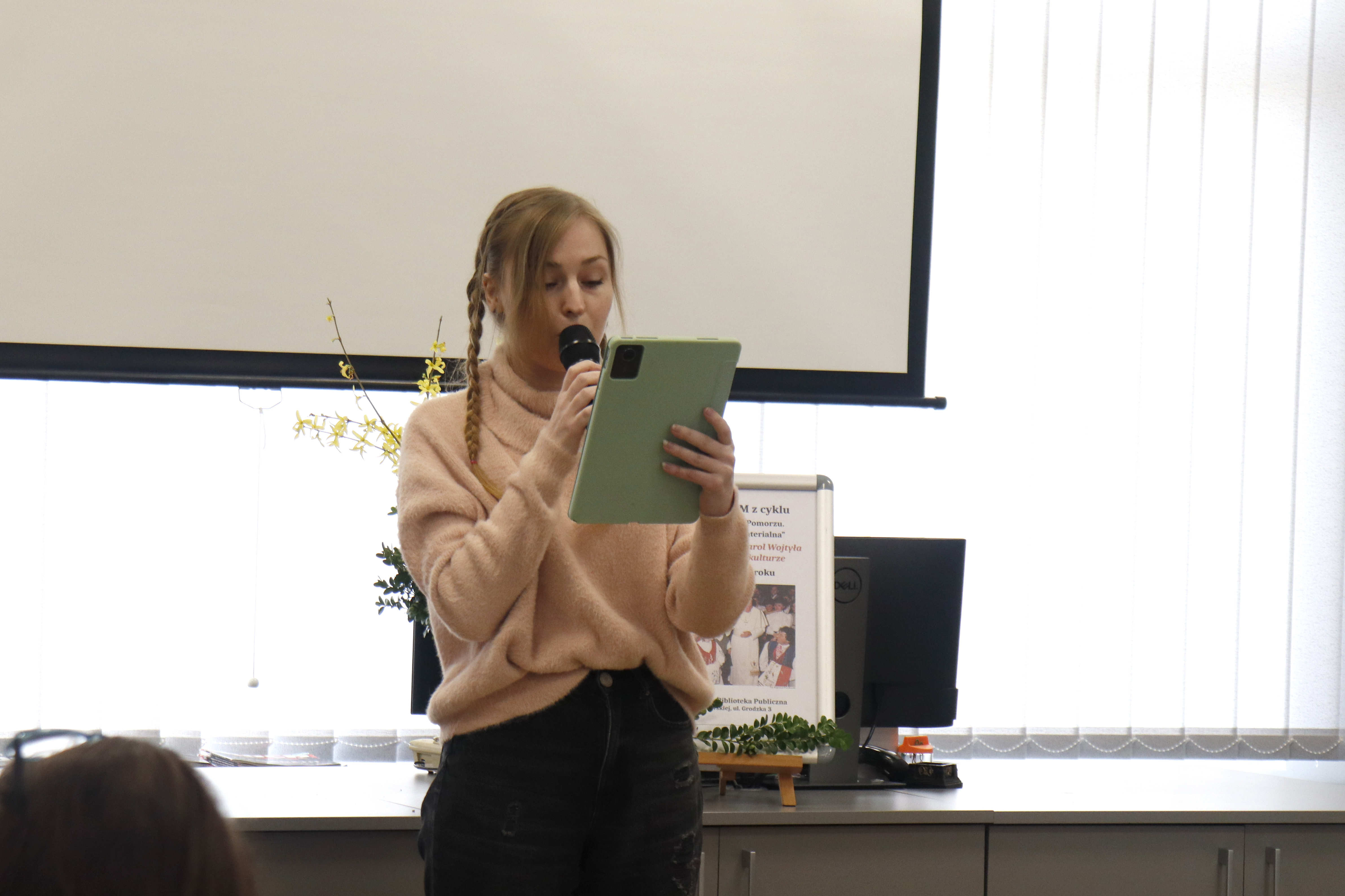 kobieta trzymająca przy ustach mikrofon i czytająca z tabletu