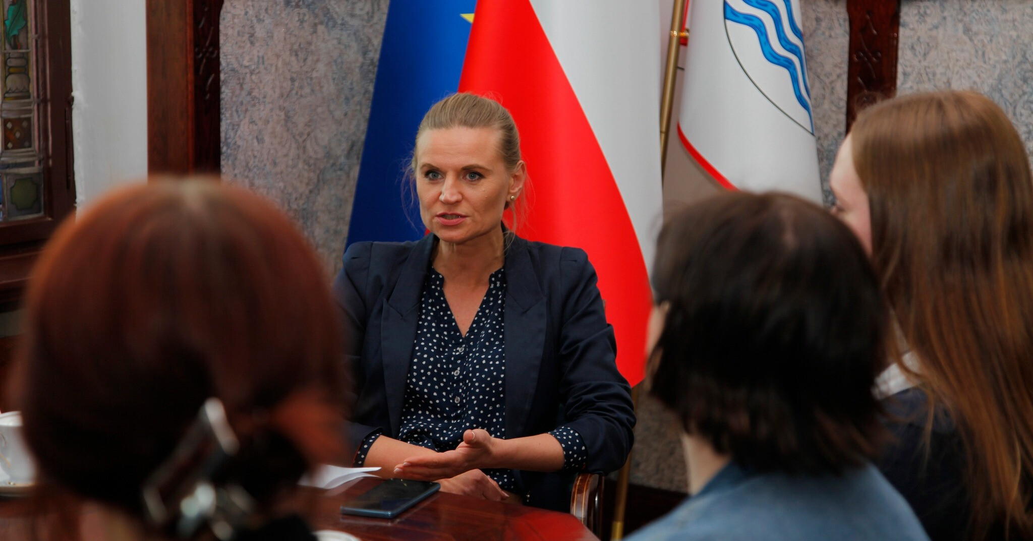 na zdjęciu na pierwszym planie zamazane głowy ludzi tyłem, w centrum zdjęcia siedząca wiceprezydentka Słupska Marta Makuch