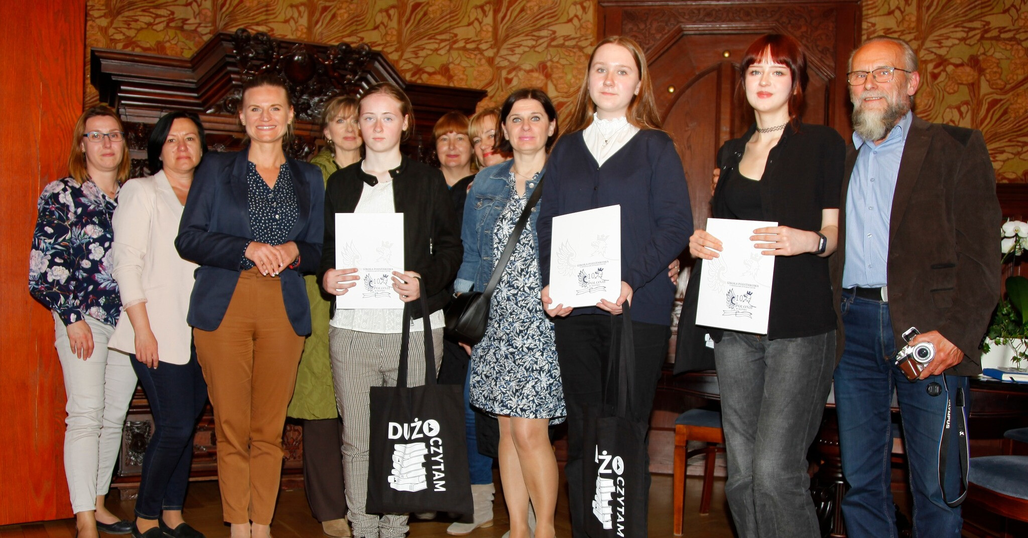 Na zdjęciu stoi grupa ludzi, laureatki konkursu razem z rodzicami, patrzą w obiektyw i niektórzy się uśmiechają