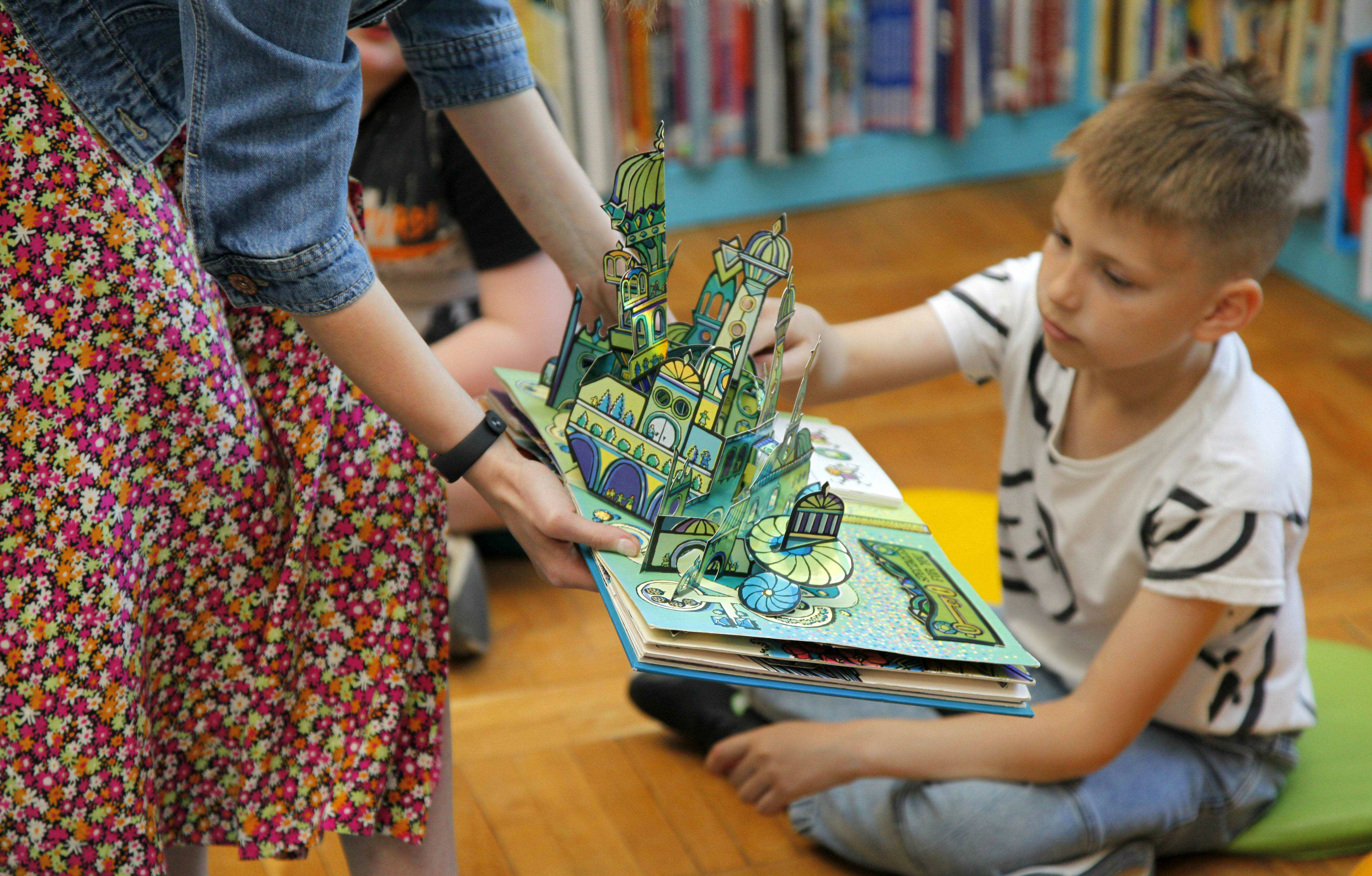 bibliotekarka prezentuje chłopcu książkę z rozkładaną ilustracją