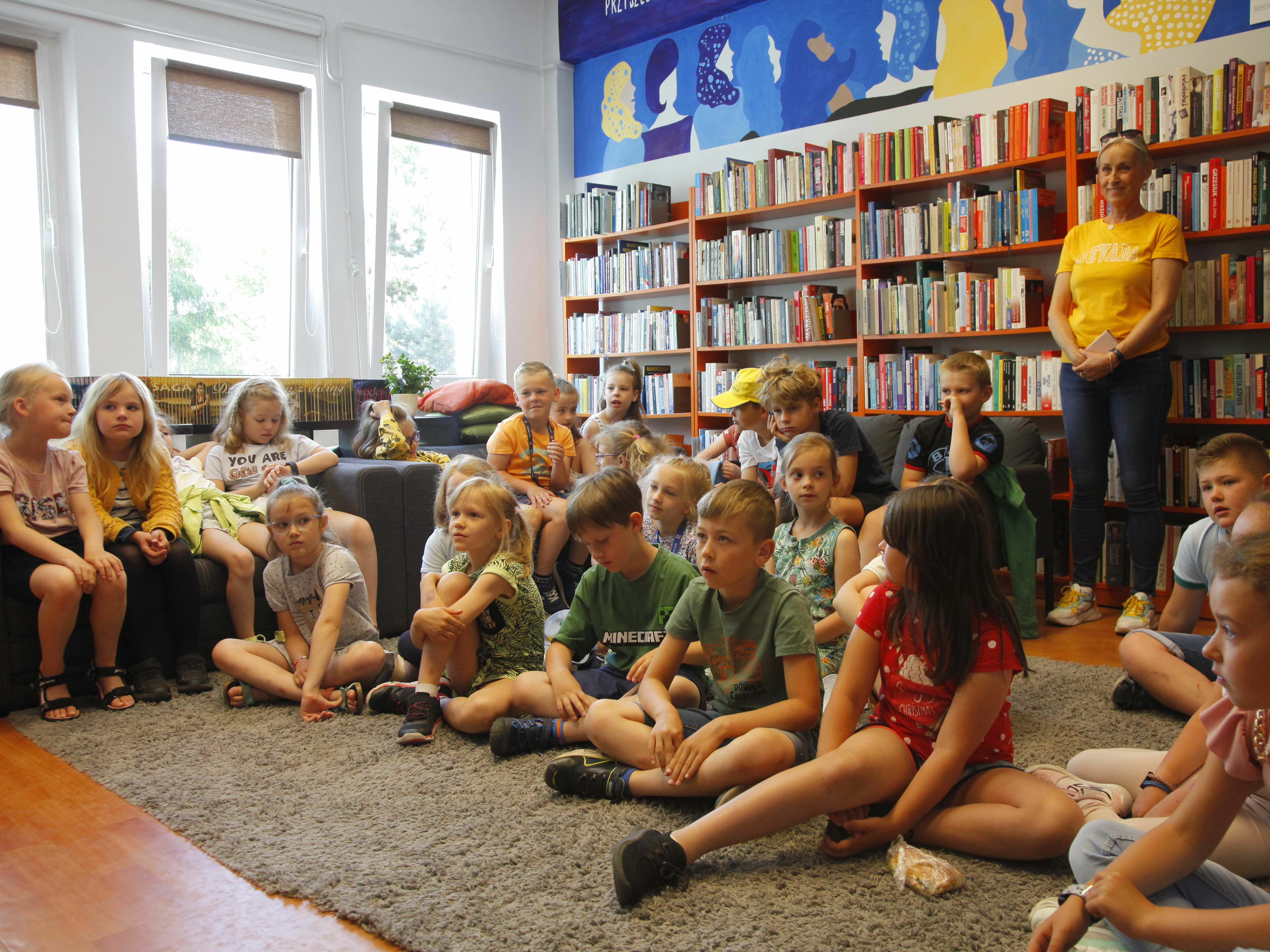 Konkurs Recytatorski - Dzieci siedzące na kanapach, na podłodze, patrzą w stonę prowadzących spotkanie