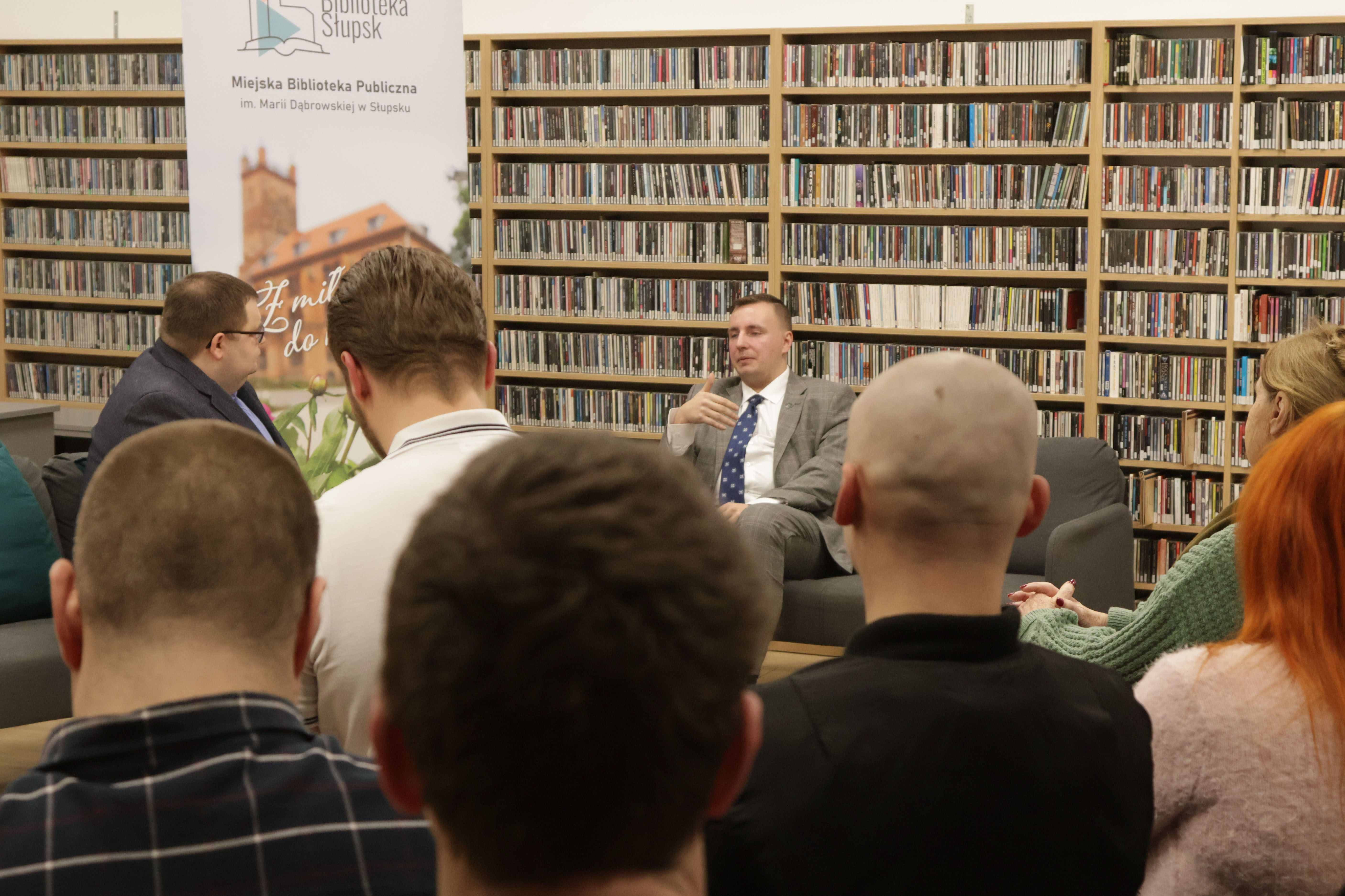 Łukasz Suchanowski wraz z prowadzącym, Szymonem Smętkiem siedzący na kanapach i rozmawiający, na pierwszym planie osoby odwrócone plecami do obiektywu