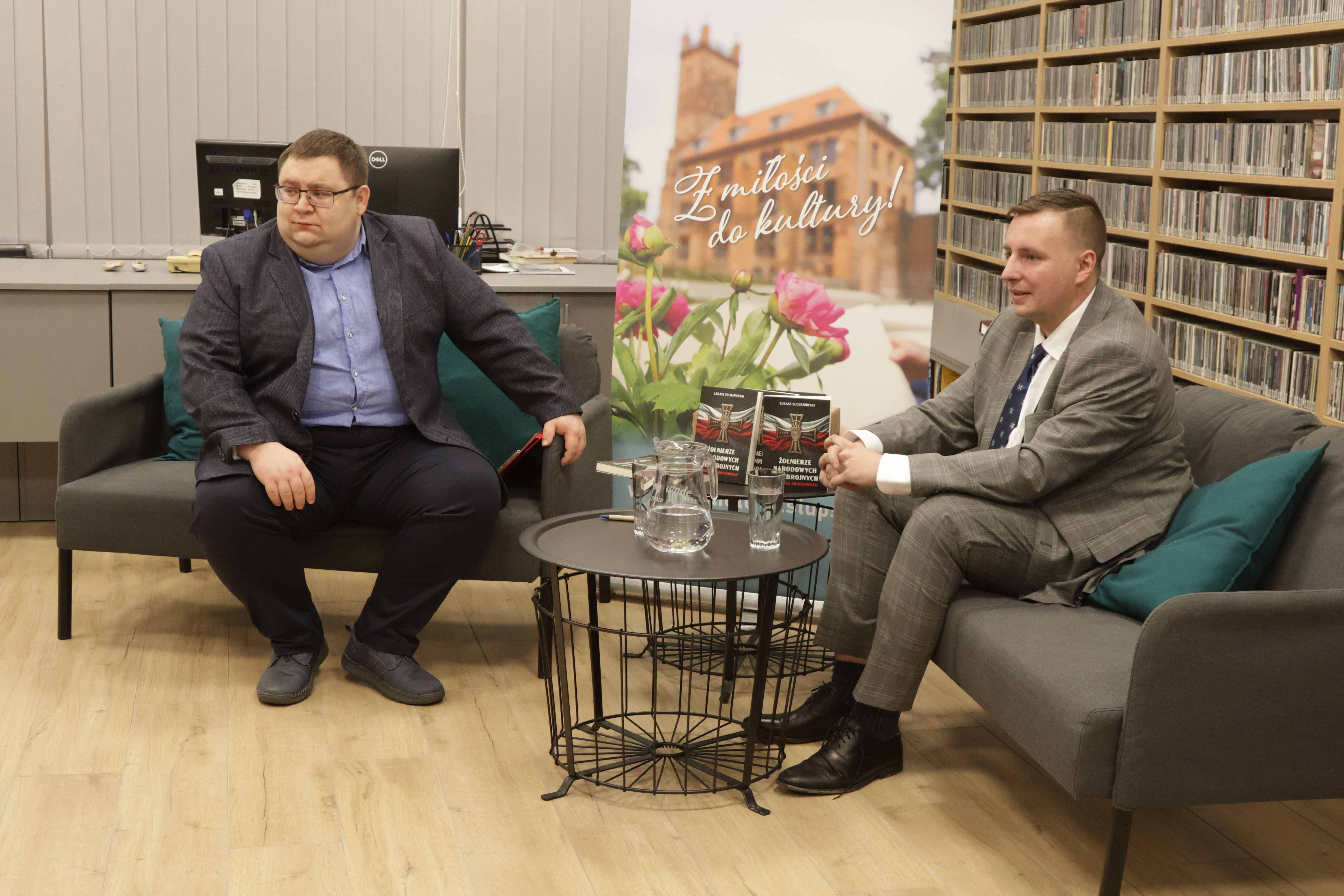 Łukasz Cuchanowski wraz z prowadzącym, Szymonem Smętkiem siedzący na kanapach i rozmawiający